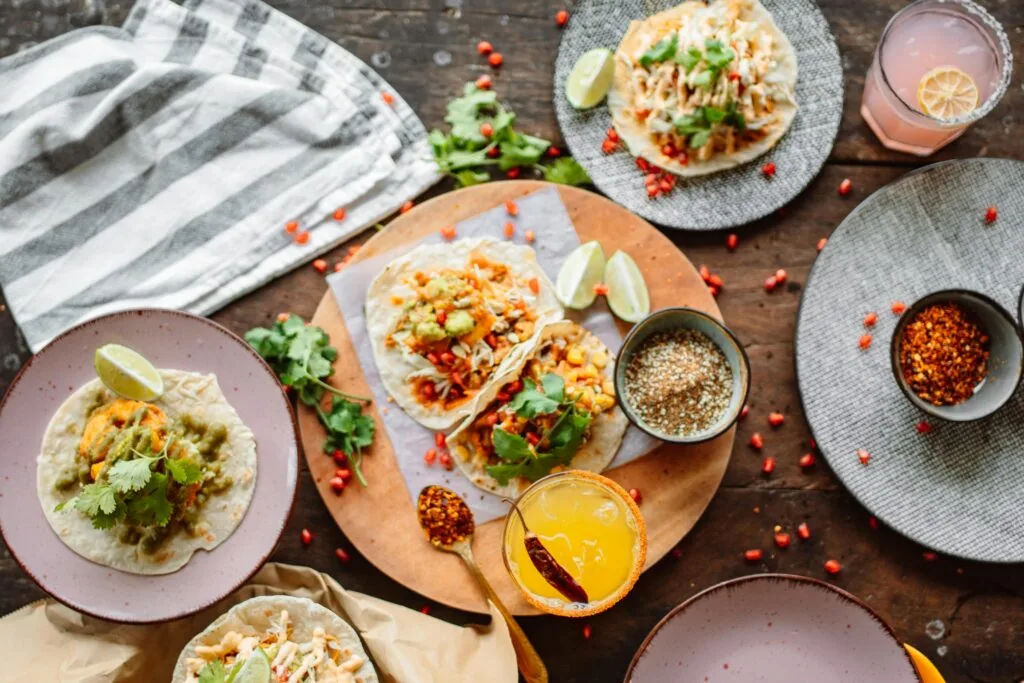Gedeckter Holztisch mit Tacos, Limetten, Koriander und Getränken von oben